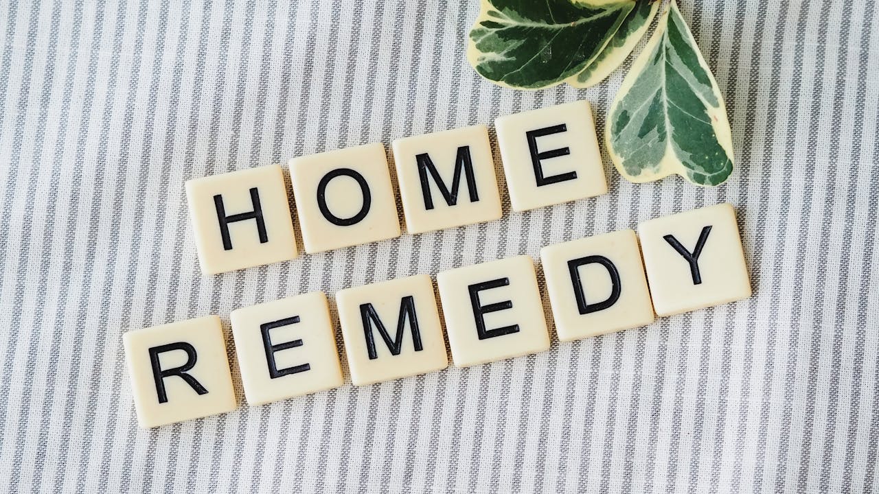 Scrabble tiles forming 'Home Remedy' with green leaves on a striped background.